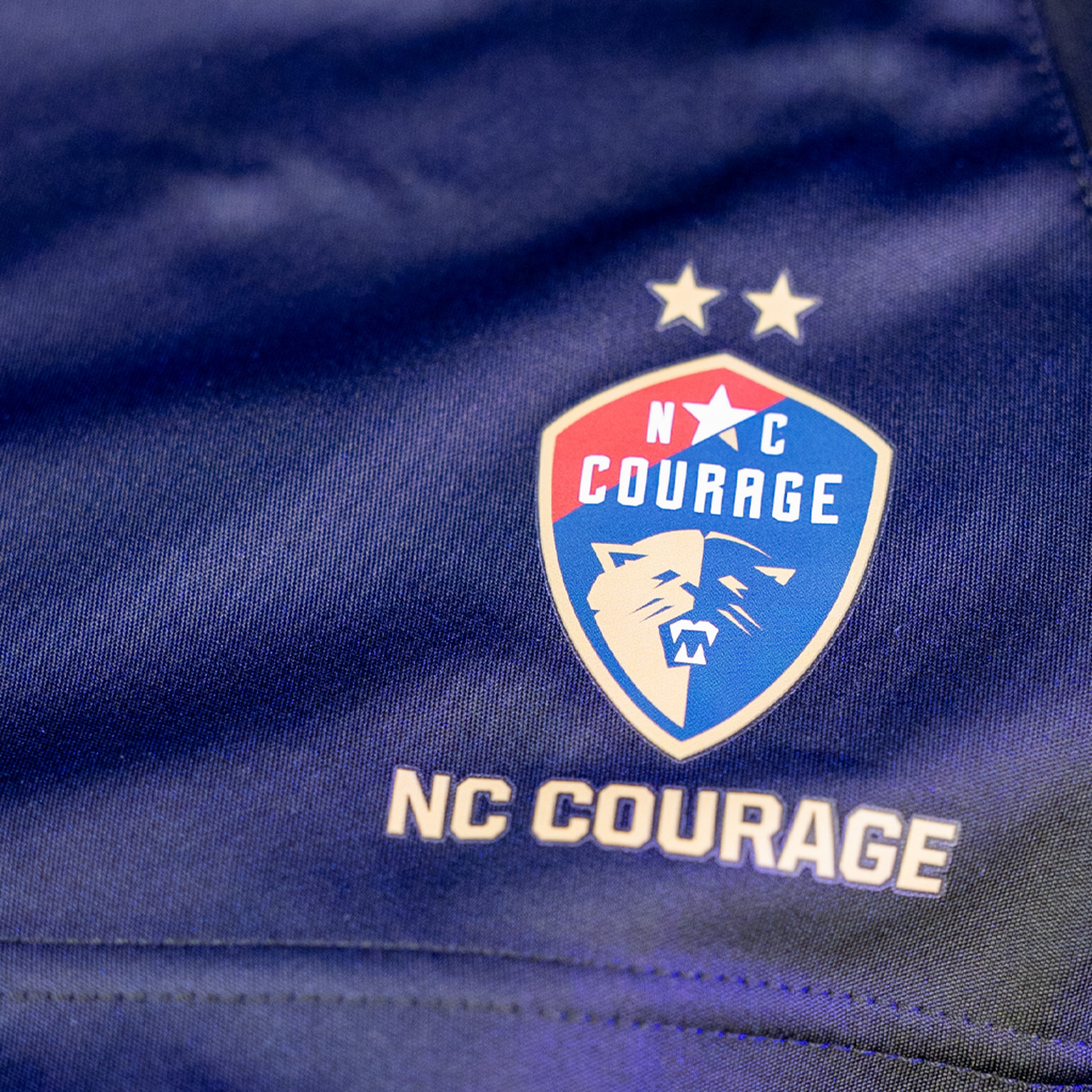A zoom in of the navy sports shorts with the Courage logo.