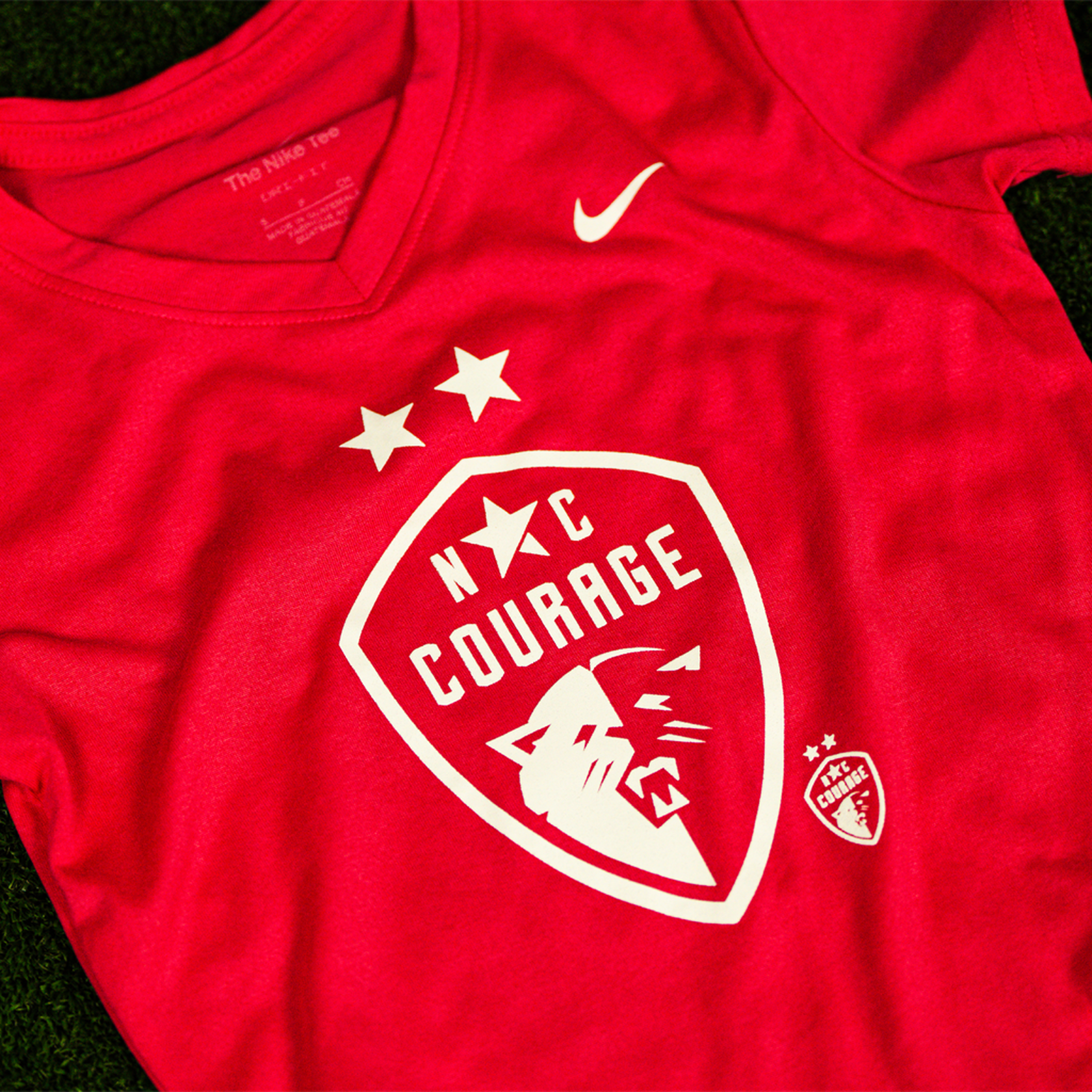 A close up of a youth-sized pink t-shirt with the NC Courage logo and Nike swoosh emblem on the front.