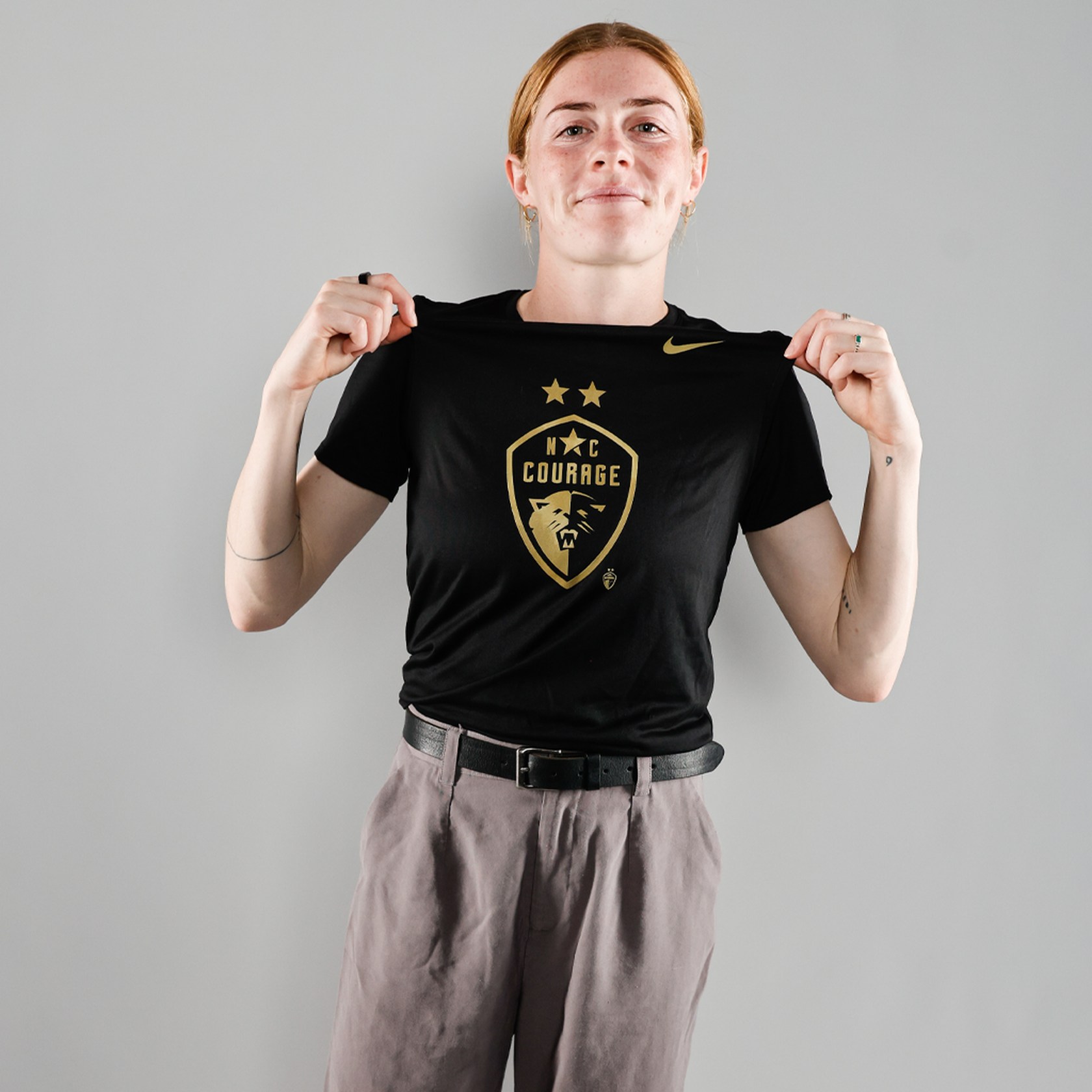 Cortnee Vine models a black t-shirt with the 'NC Courage' logo in gold and black, featuring Nike branding as well.