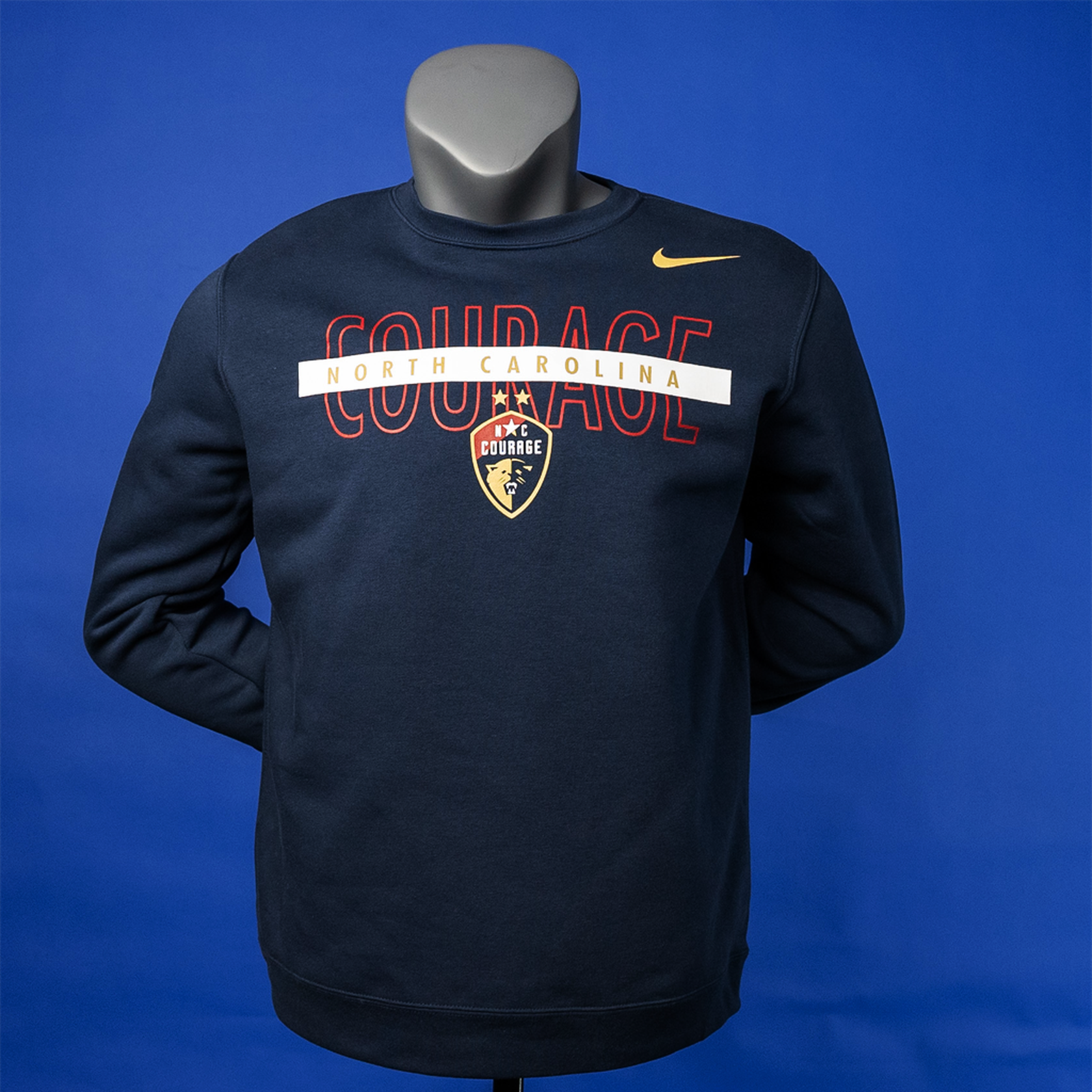 A navy blue crewneck sweatshirt with the NC Courage logo and the word ' COURAGE ' written across the chest in bold letters.