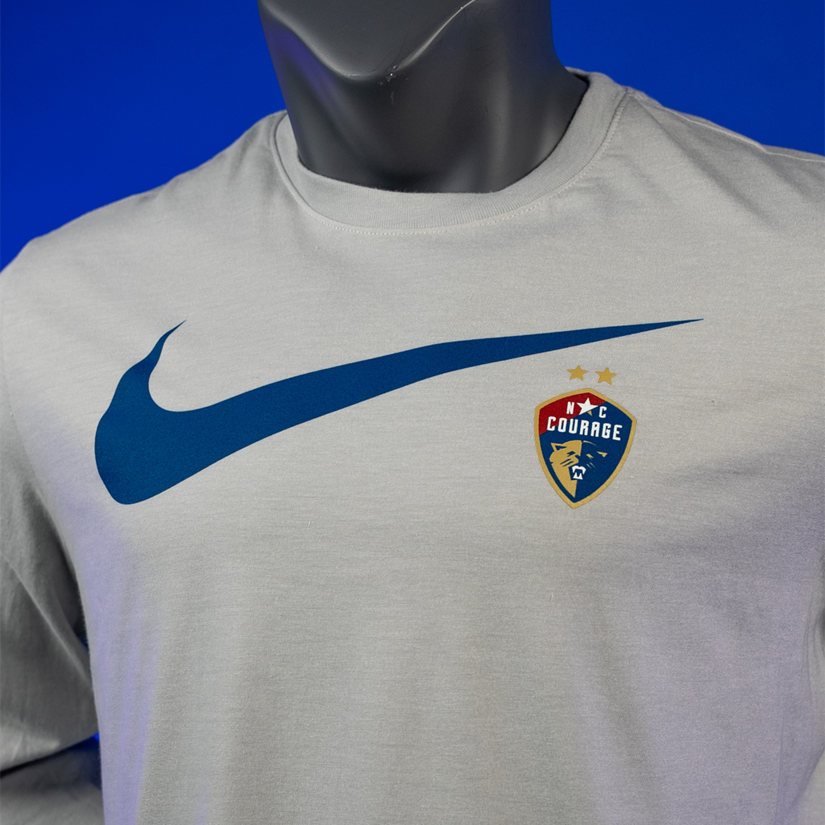 A zoomed-in long sleeve white t-shirt featuring the Nike Swoosh logo in blue and the NC Courage logo on the left chest area.