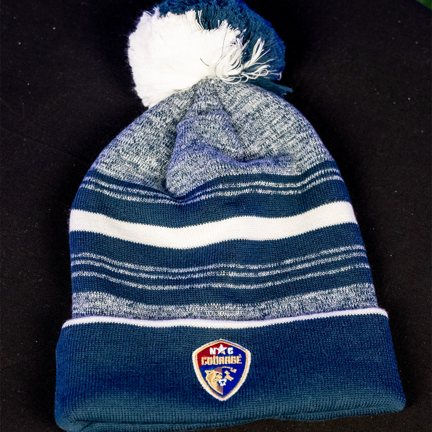A navy and white striped beanie with a pom-pom on top, featuring the NC Courage logo.