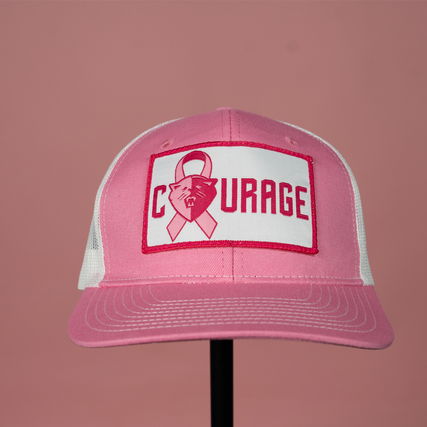 A pink and white trucker hat with the NC Courage logo and the word 'COURAGE' on a patch on the front.