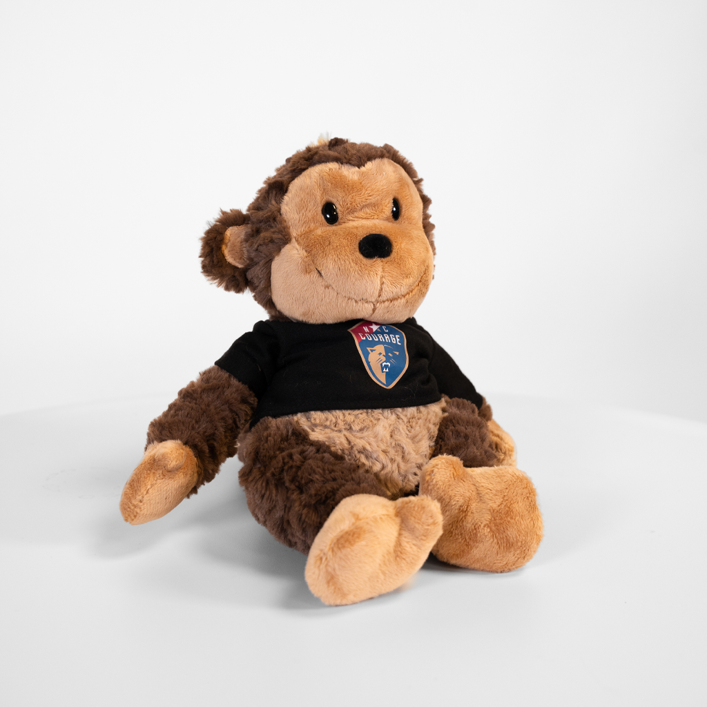 Four plush toy animals, including a bear, a pink pig, a wolf, and a dog, each wearing a black shirt with a logo, seated in a row on a white surface against a neutral background.