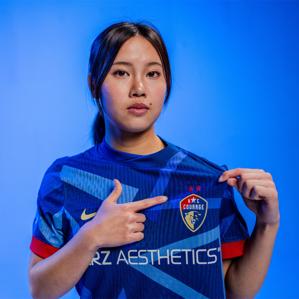 Manaka wearing 2025 Blue "The Belong" pointing at the North Carolina Courage crest
