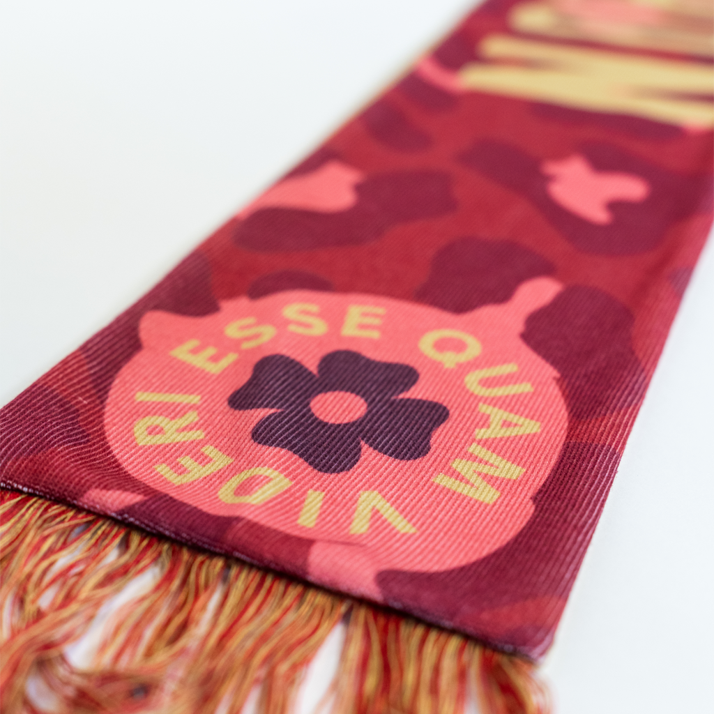 A close-up of a red and pink camouflage patterned scarf with a logo and the text "Esse Quam Videri" prominently displayed.