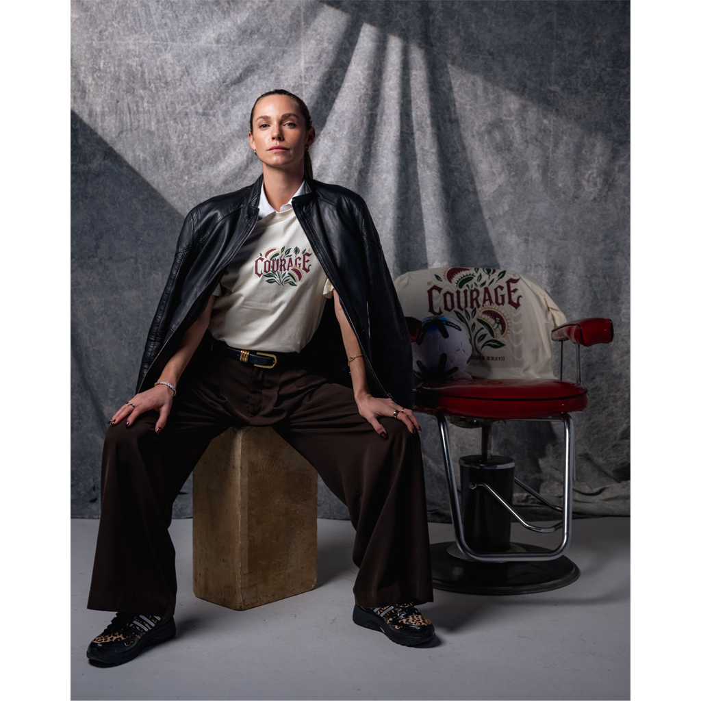 Person wearing a 'Courage' shirt sitting on a block with a chair in the background.