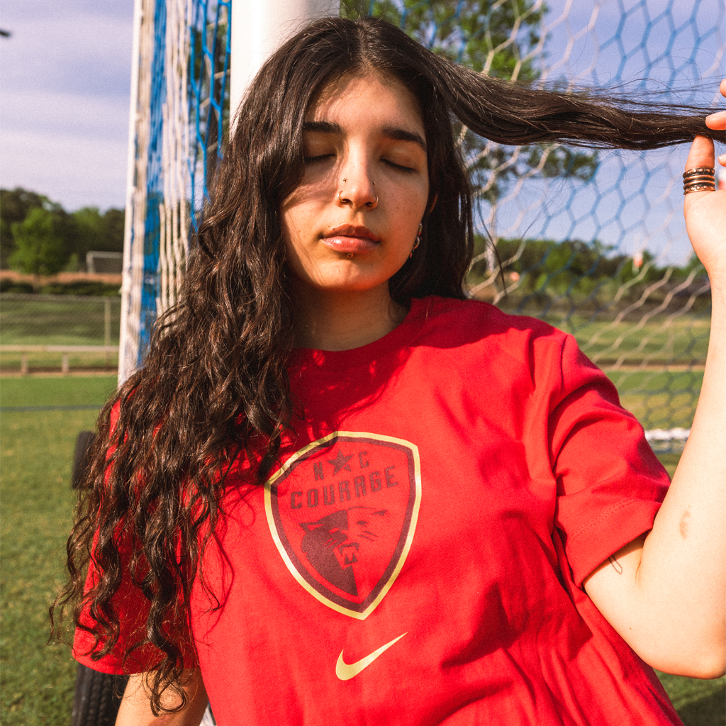 Person wearing A pink Nike t-shirt with the NC Courage crest printed on the front